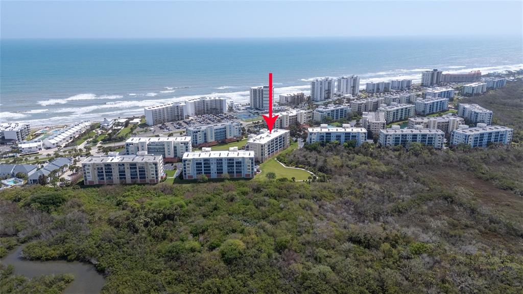An aerial view shows a multi-story apartment building marked by a red arrow near the ocean — 5300 S ATLANTIC AVENUE UNIT 6-207, NEW SMYRNA BEACH, FL