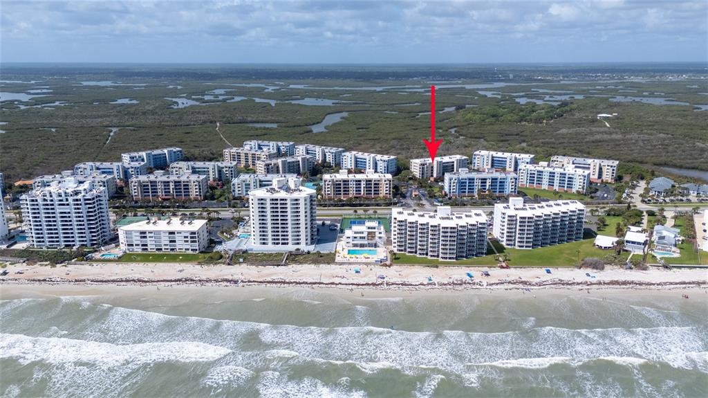 An aerial view shows a coastal condominium complex with a red arrow pointing toward one building — 5300 S ATLANTIC AVENUE UNIT 6-207, NEW SMYRNA BEACH, FL