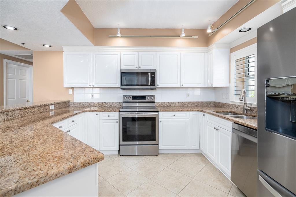 A kitchen features white cabinets, granite countertops, stainless steel appliances, and light-colored tile flooring — 5300 S ATLANTIC AVENUE UNIT 6-207, NEW SMYRNA BEACH, FL
