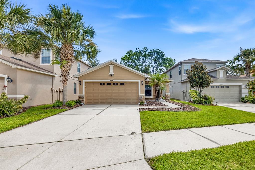 A tan single-story house with a two-car garage and a concrete driveway — 7861 TUSCANY WOODS DRIVE, TAMPA, FL