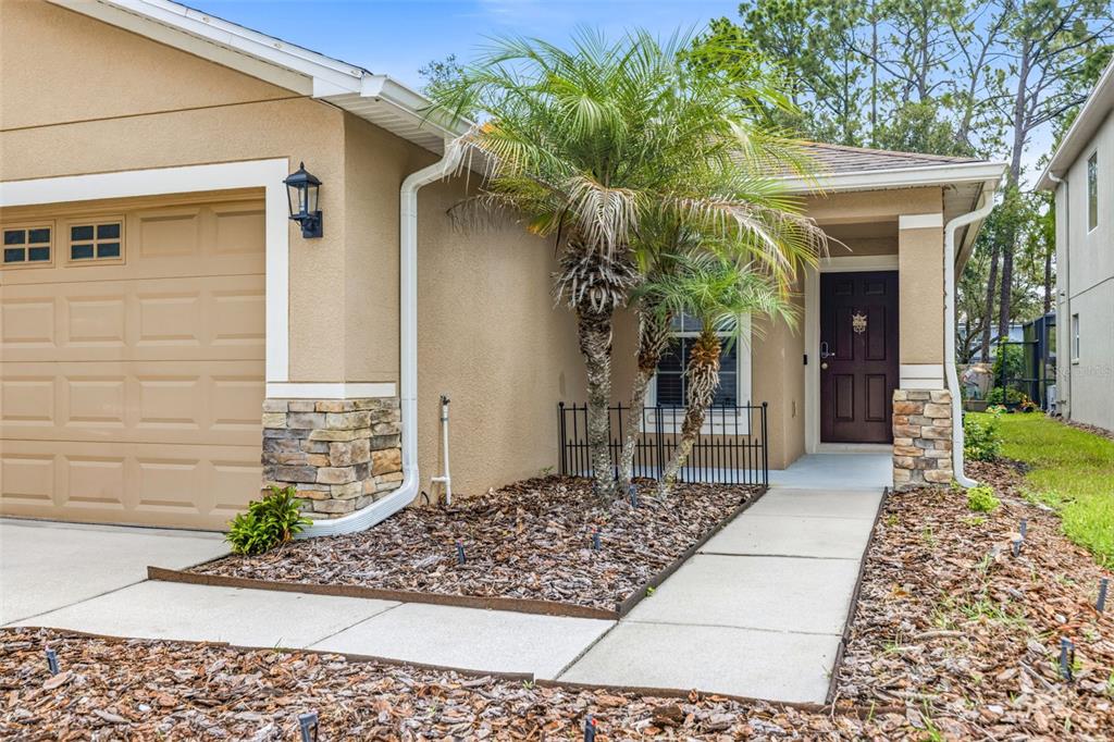 A tan house exterior features a garage, a front door, and a small palm tree — 7861 TUSCANY WOODS DRIVE, TAMPA, FL