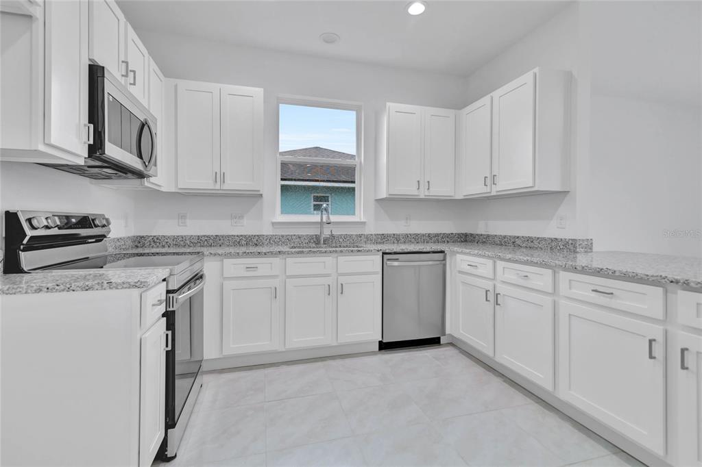 A kitchen features white cabinets, granite countertops, stainless steel appliances, and light-colored tile flooring — 3788 WATERCLIFF CIRCLE, GRAND ISLAND, FL