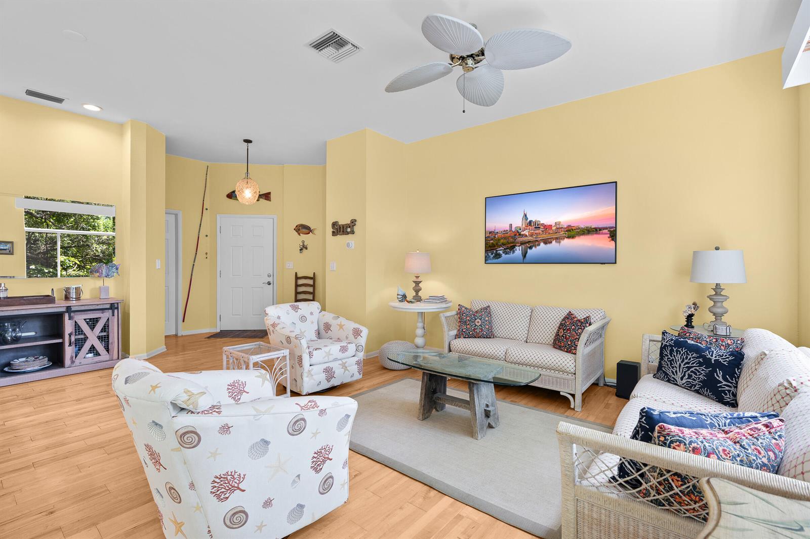 A living room with yellow walls, wicker furniture, a ceiling fan, and a wall-mounted television — VERO BEACH, FL