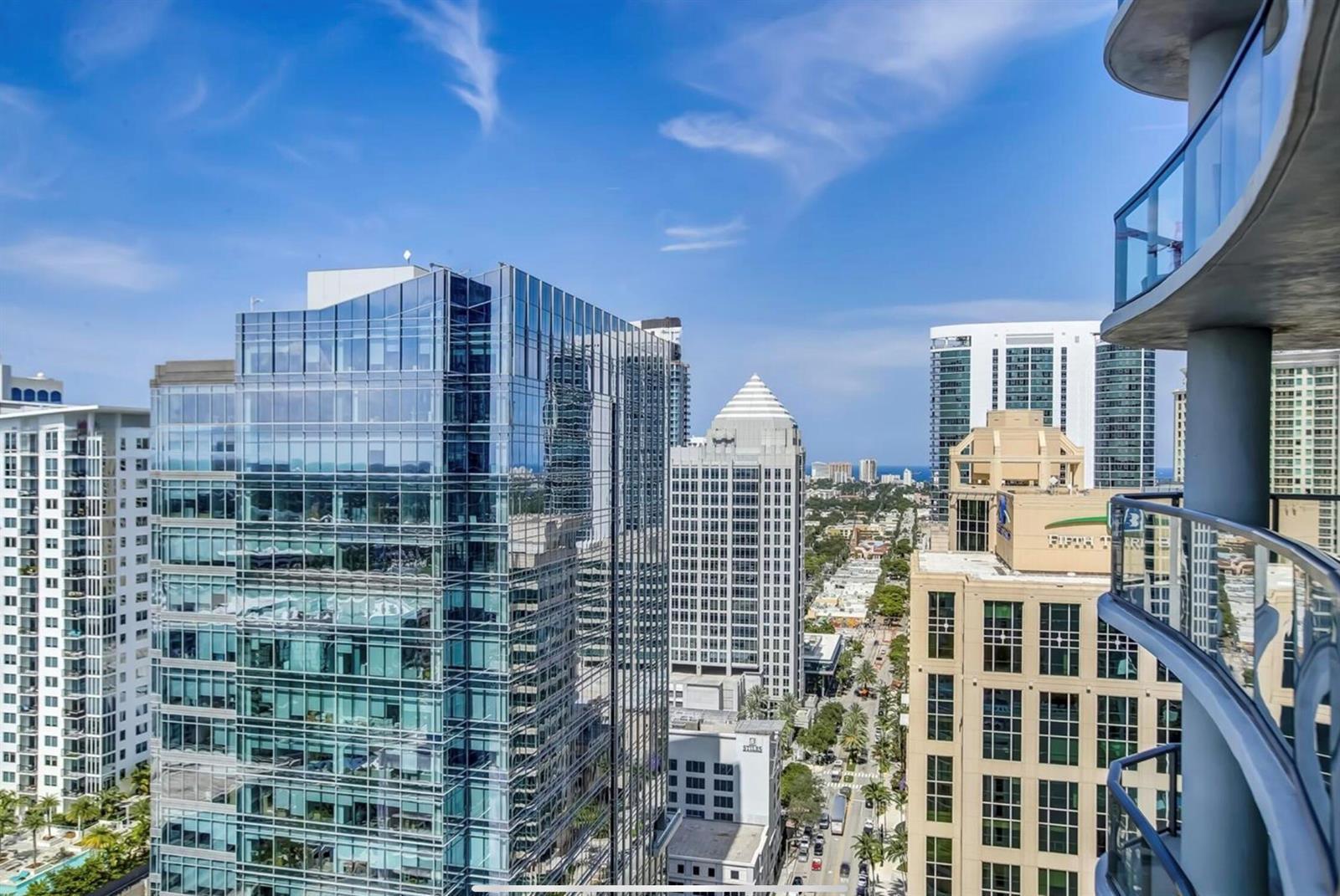 A high-angle view of a city skyline featuring modern glass skyscrapers and a balcony railing — 100 E Las Olas Boulevard # 2802, Fort Lauderdale FL 33301, FORT LAUDERDALE, FL