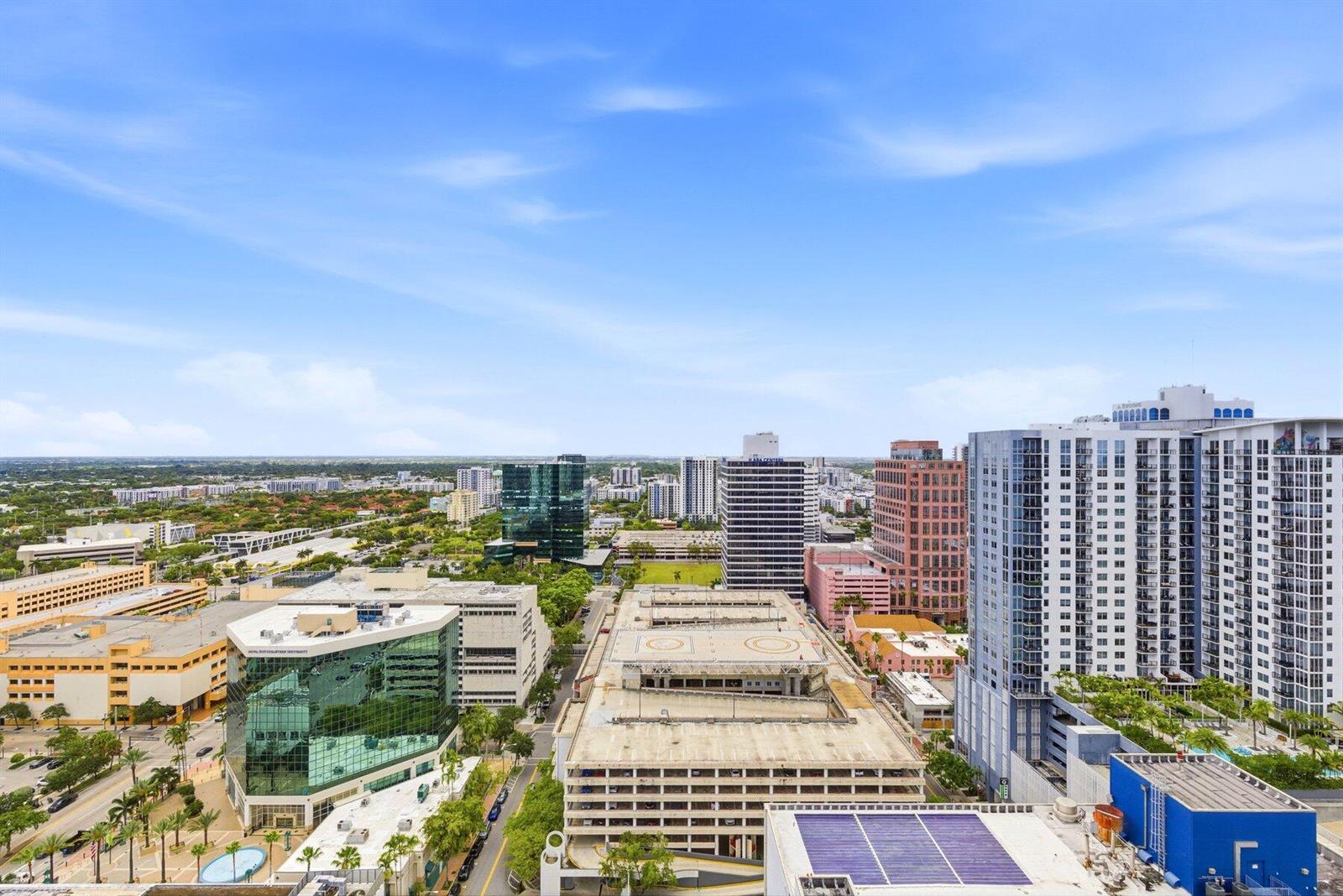 An elevated view of a city skyline featuring office buildings, parking garages, and palm trees — 100 E Las Olas Boulevard # 2802, Fort Lauderdale FL 33301, FORT LAUDERDALE, FL