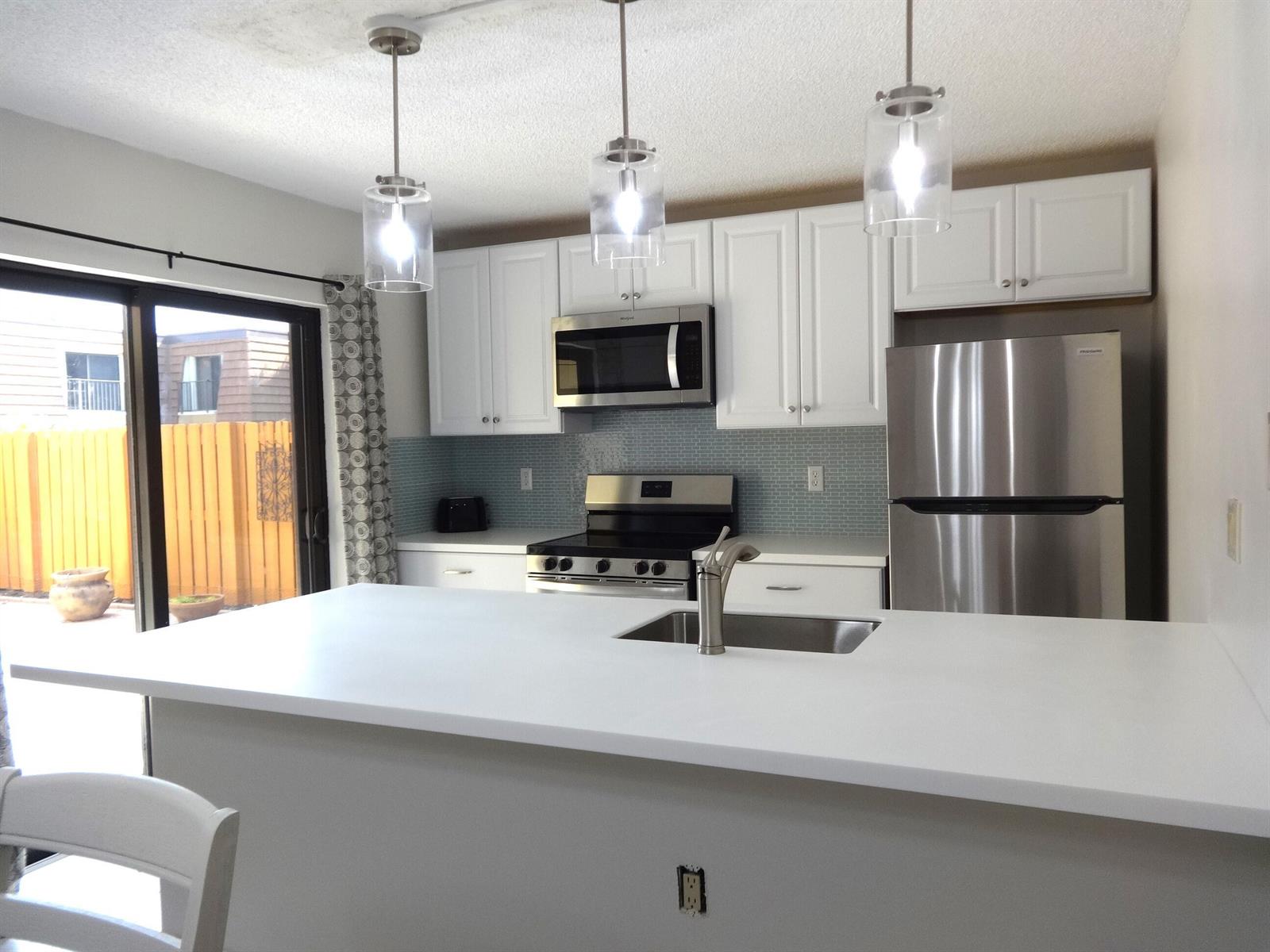 A kitchen features white cabinets, stainless steel appliances, a center island with a sink, and backsplash — 2914 29th Court, Jupiter FL 33477, JUPITER, FL