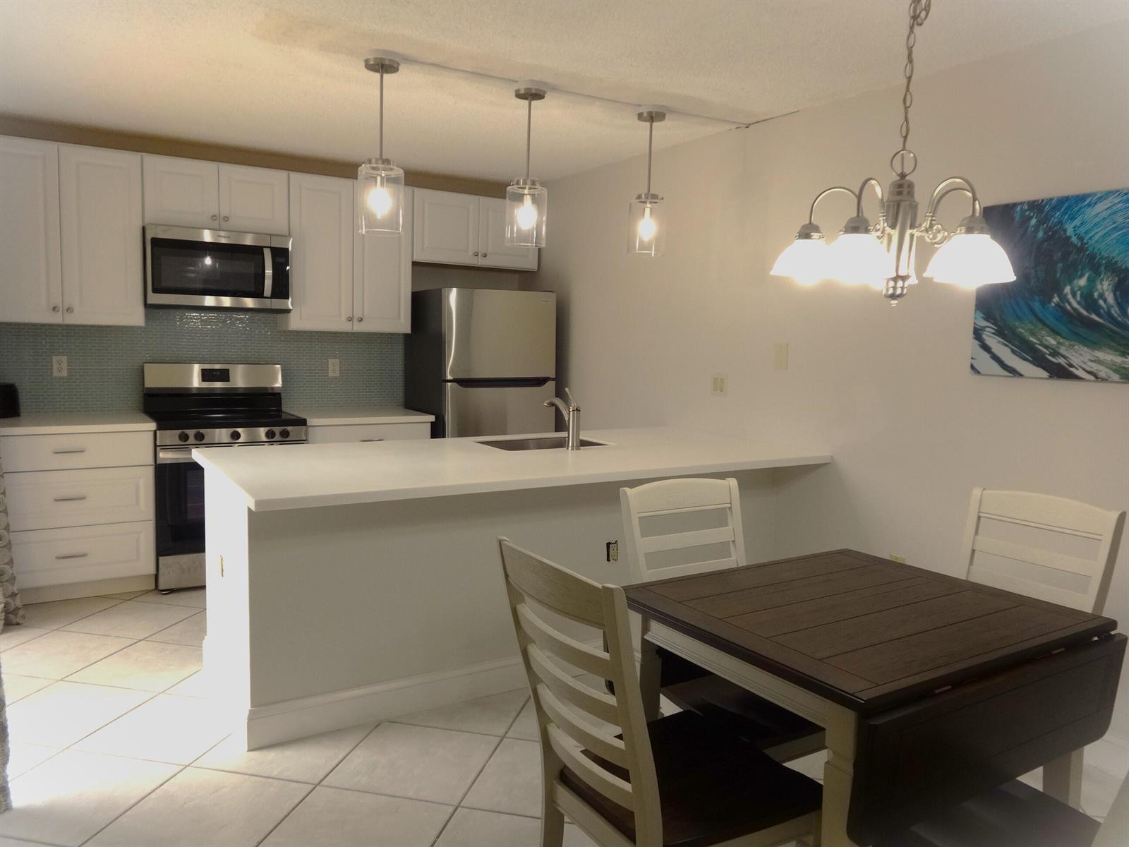 A kitchen with white cabinets, stainless steel appliances, a breakfast bar, and a dining area — 2914 29th Court, Jupiter FL 33477, JUPITER, FL