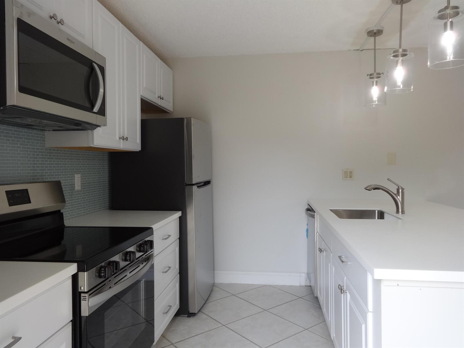 A kitchen features white cabinets, stainless steel appliances, a tiled backsplash, and a peninsula sink — 2914 29th Court, Jupiter FL 33477, JUPITER, FL
