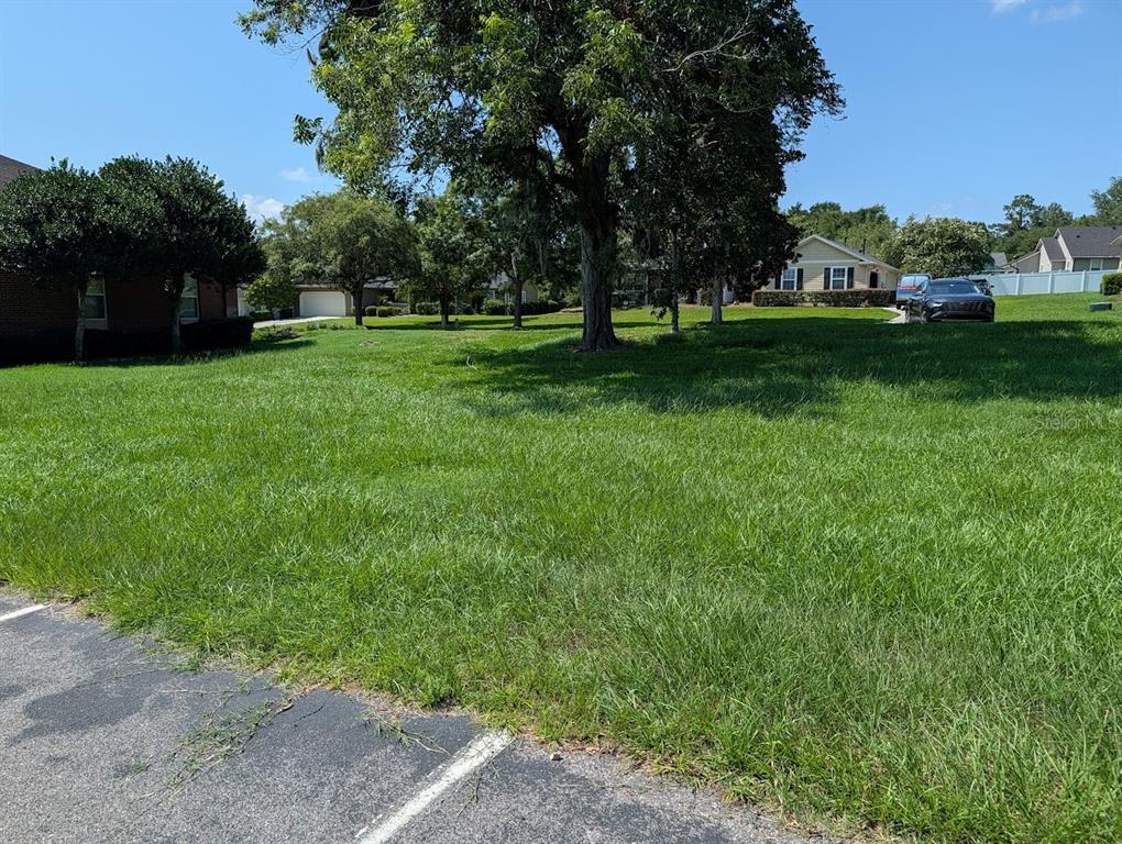 A grassy vacant lot sits between residential houses under a clear blue sky — Lot 00 NW 151ST BOULEVARD, ALACHUA, FL