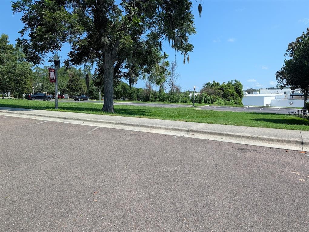 A paved parking lot sits adjacent to a grassy area with trees and a sidewalk — Lot 00 NW 151ST BOULEVARD, ALACHUA, FL