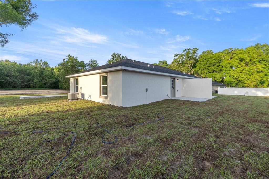 The exterior of a light-colored, single-story house features a small concrete patio and lawn — 5349 NW 11TH STREET, OCALA, FL
