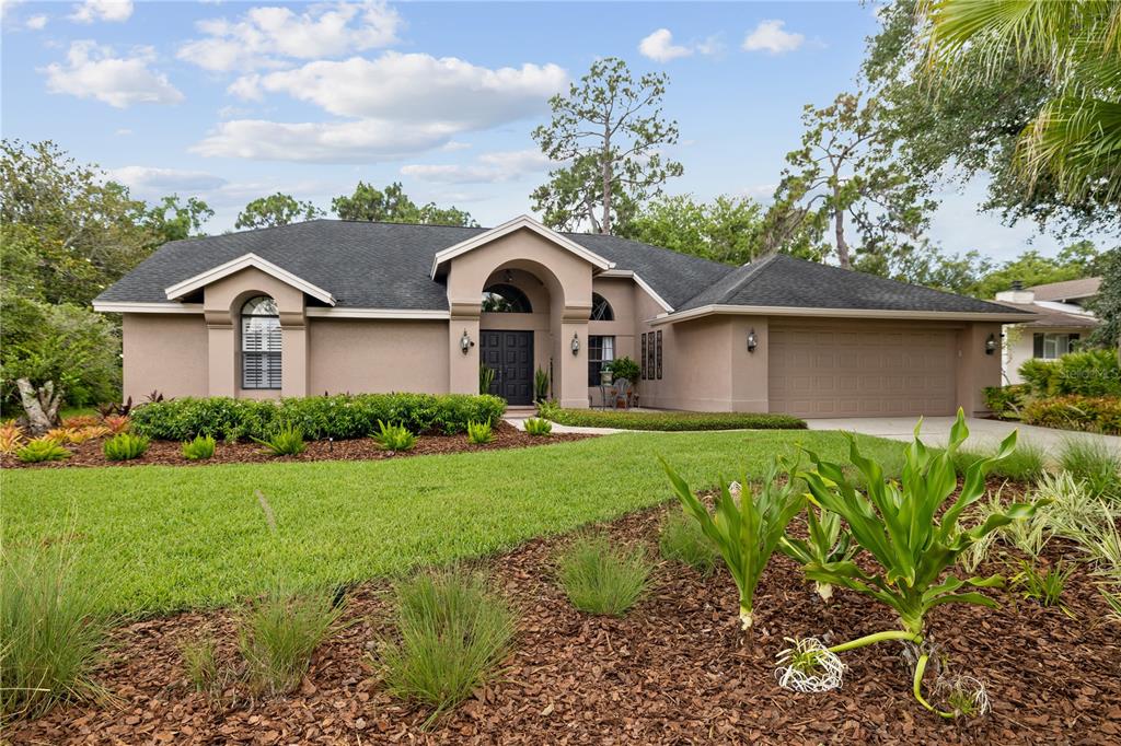 A single-story house with a tan stucco exterior, dark roof, and a two-car garage — 3372 BRIAN ROAD S, PALM HARBOR, FL