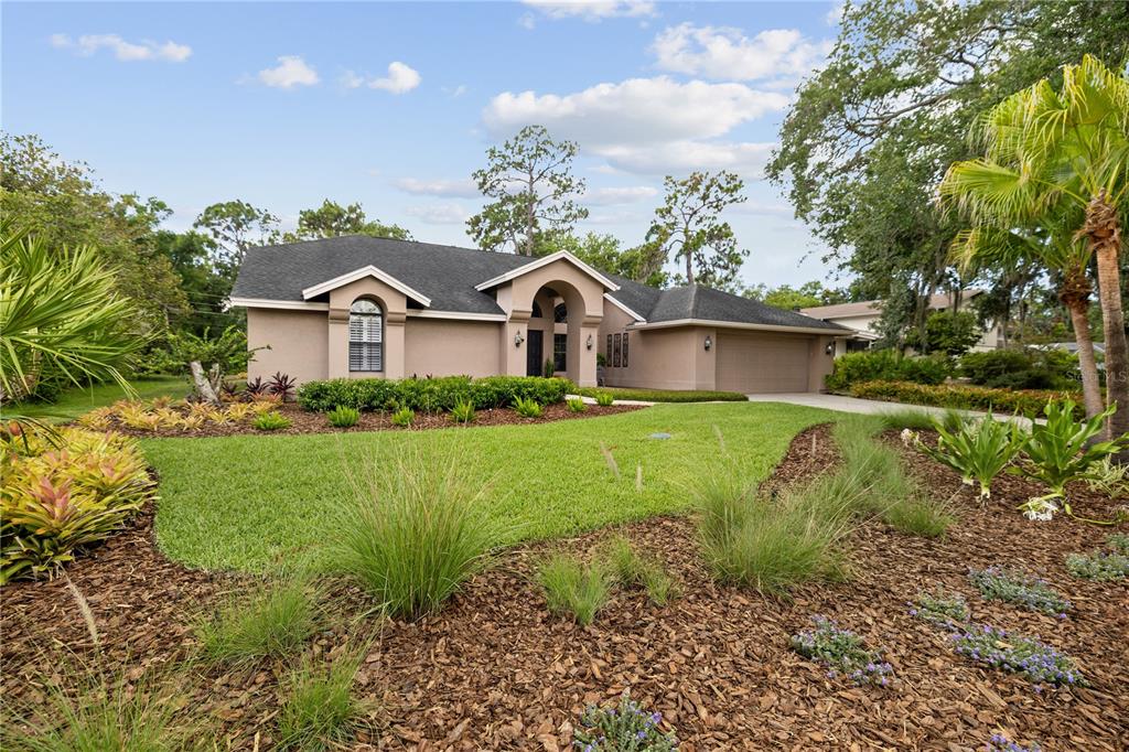A single-story tan house with a dark shingled roof and a landscaped front yard — 3372 BRIAN ROAD S, PALM HARBOR, FL