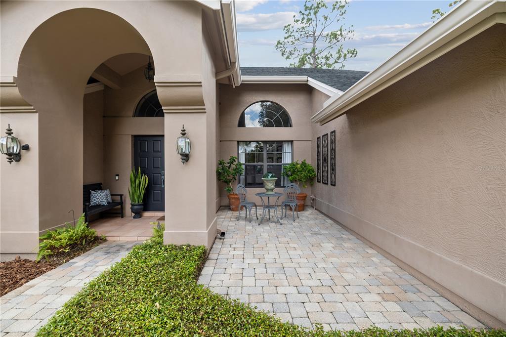 A paved courtyard leads to a front entrance with a dark door and arched alcove — 3372 BRIAN ROAD S, PALM HARBOR, FL