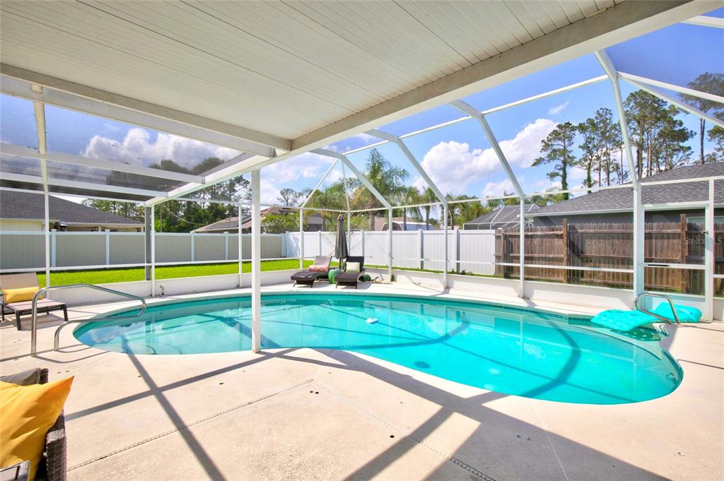 A screened-in swimming pool with a concrete deck and a white fence in the background — 33 RIVERSIDE LANE, PALM COAST, FL