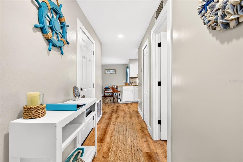 A hallway with wood-look flooring leads toward a kitchen featuring white cabinets and bar seating — 33 RIVERSIDE LANE, PALM COAST, FL