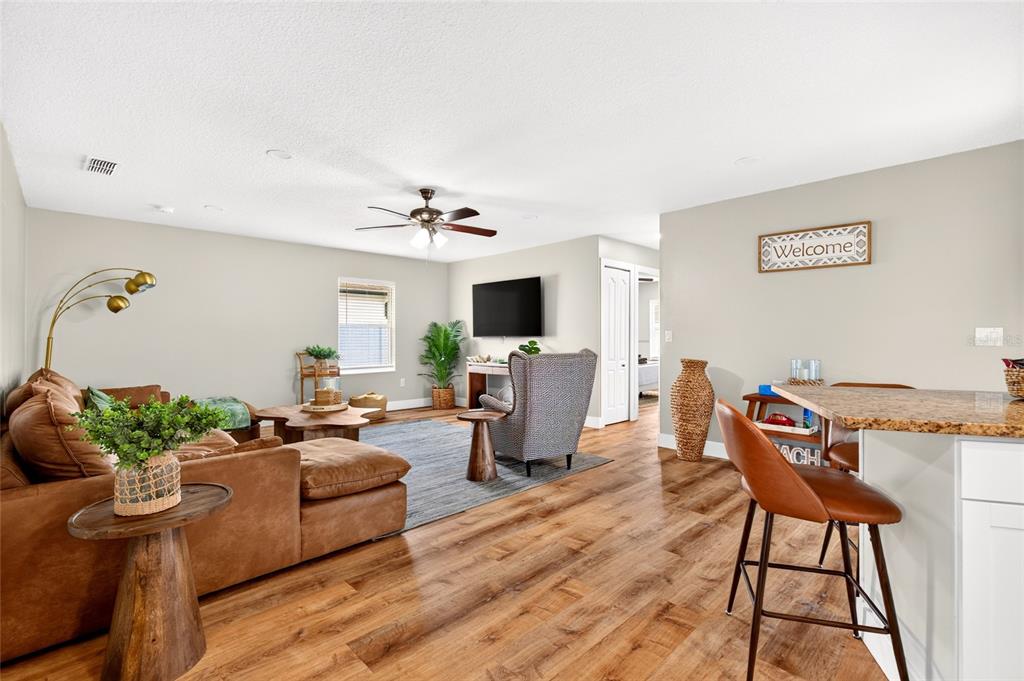 A living room with wood-look flooring, a brown sectional sofa, and an open kitchen area — 33 RIVERSIDE LANE, PALM COAST, FL