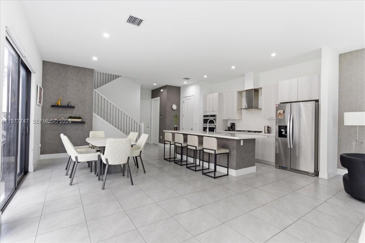 A modern open-concept kitchen and dining area features white cabinetry, a central island, and stairs — 4395 NW 80th Ct, Doral FL 33166, DORAL, FL