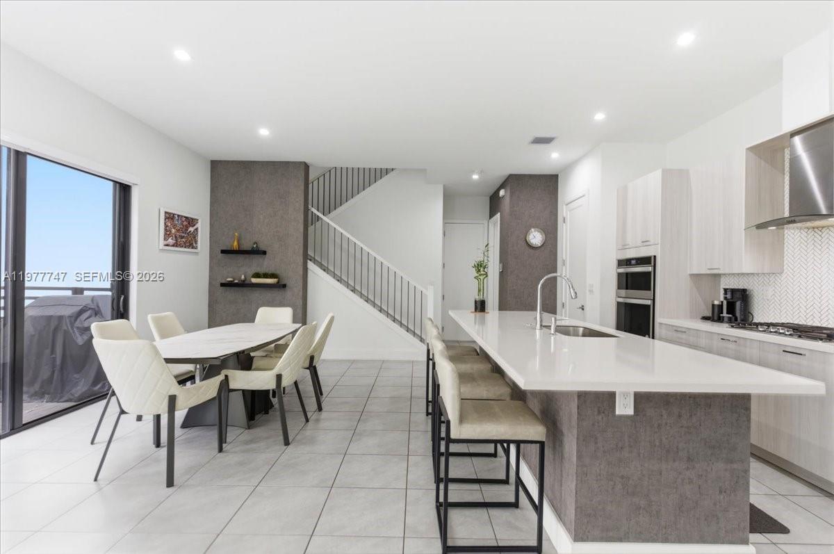 A modern open-concept kitchen and dining area features a large island, tile flooring, and stairs — 4395 NW 80th Ct, Doral FL 33166, DORAL, FL