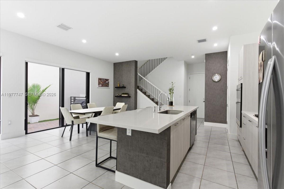 A modern kitchen features a large quartz island, light wood cabinetry, and a dining area — 4395 NW 80th Ct, Doral FL 33166, DORAL, FL