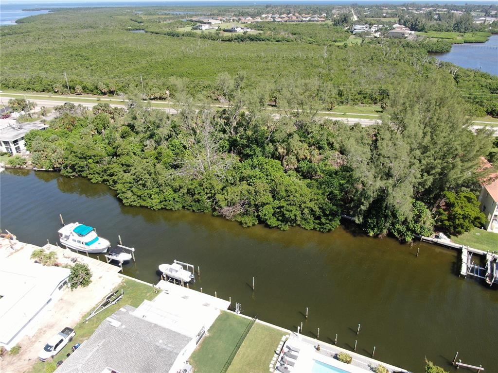 An aerial view shows a canal with docked boats bordering a dense wooded area — 10005 W MANATEE AVENUE W, BRADENTON, FL
