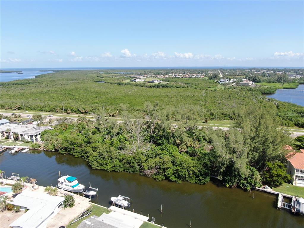 An aerial view shows a canal with boats, dense vegetation, and a distant residential neighborhood — 10005 W MANATEE AVENUE W, BRADENTON, FL