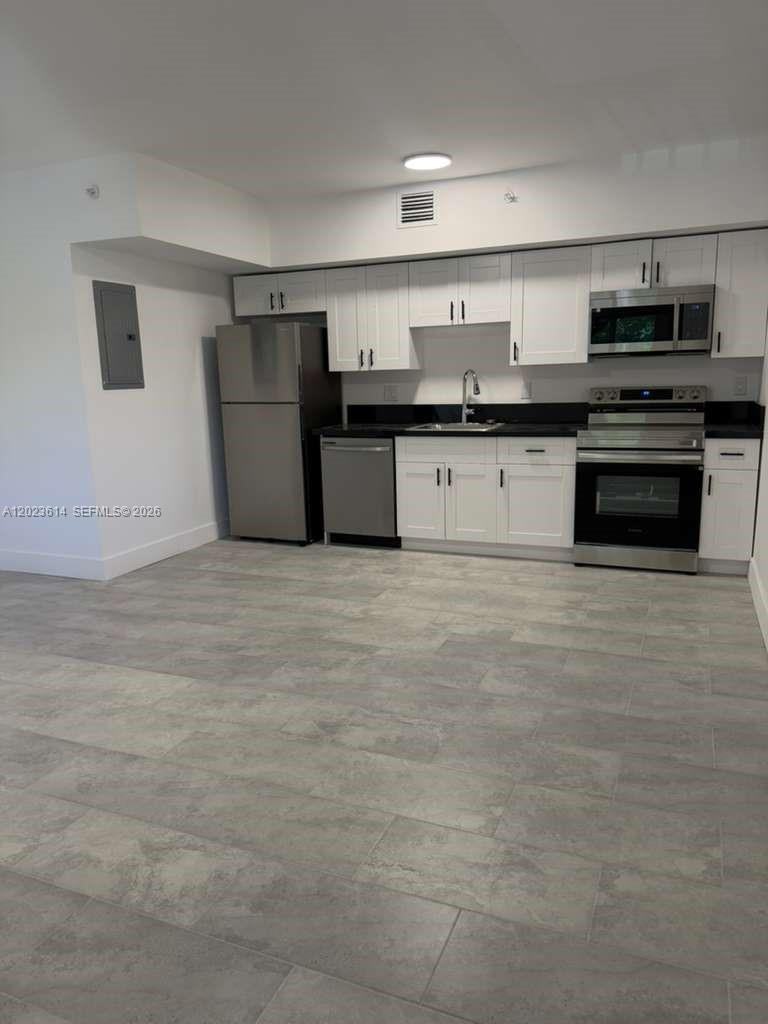 A kitchen features white cabinets, stainless steel appliances, and gray tile flooring — 147 Nw 59th St # 205, Miami FL 33127, MIAMI, FL