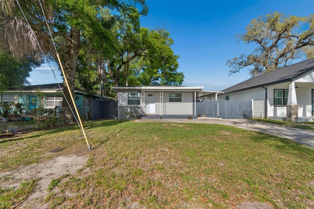 A gray single-story house with a front porch and a fenced yard under blue skies — 6710 N HARER STREET, TAMPA, FL