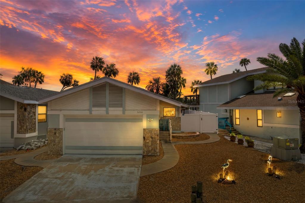 A residential house exterior with a garage and palm trees under a vibrant sunset sky — 5250 S RIVERVIEW CIRCLE, HOMOSASSA, FL