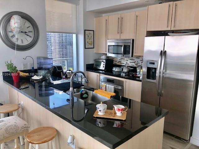 A modern kitchen features light wood cabinets, stainless steel appliances, and a black countertop island — 1111 SW 1st Ave # 3225, Miami FL 33130, MIAMI, FL