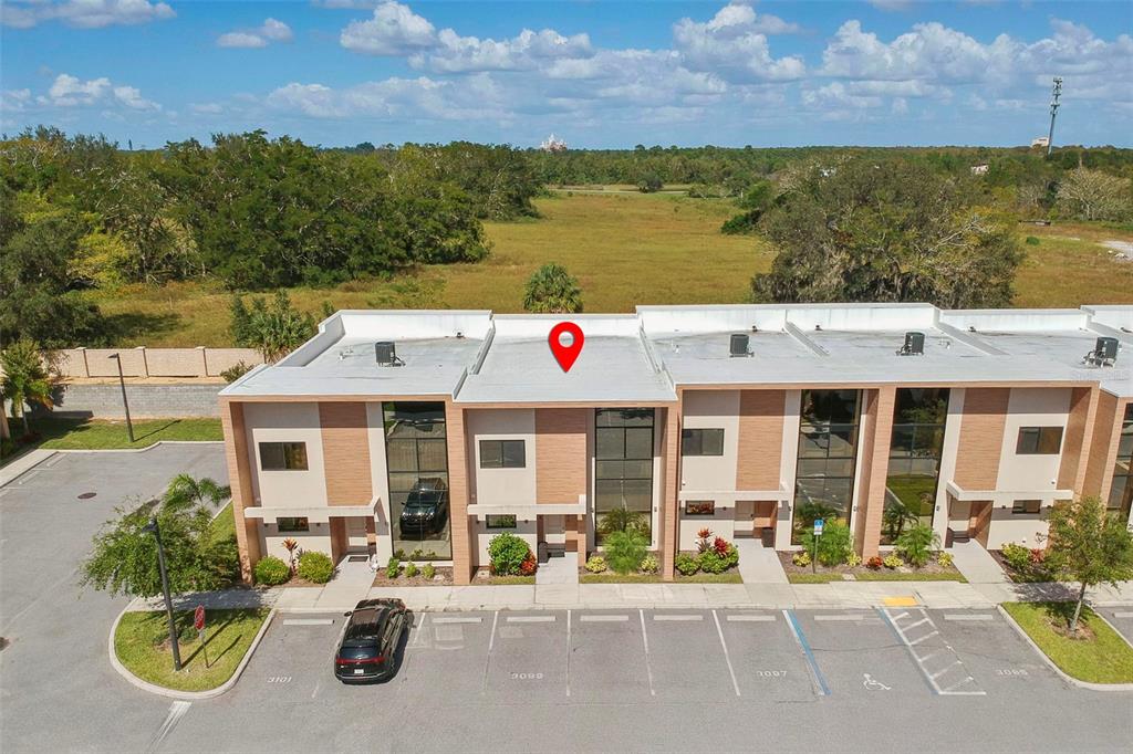 An aerial view shows a modern multi-unit townhouse building with a parking lot in front — 3099 ROCKEFELLER WAY, KISSIMMEE, FL
