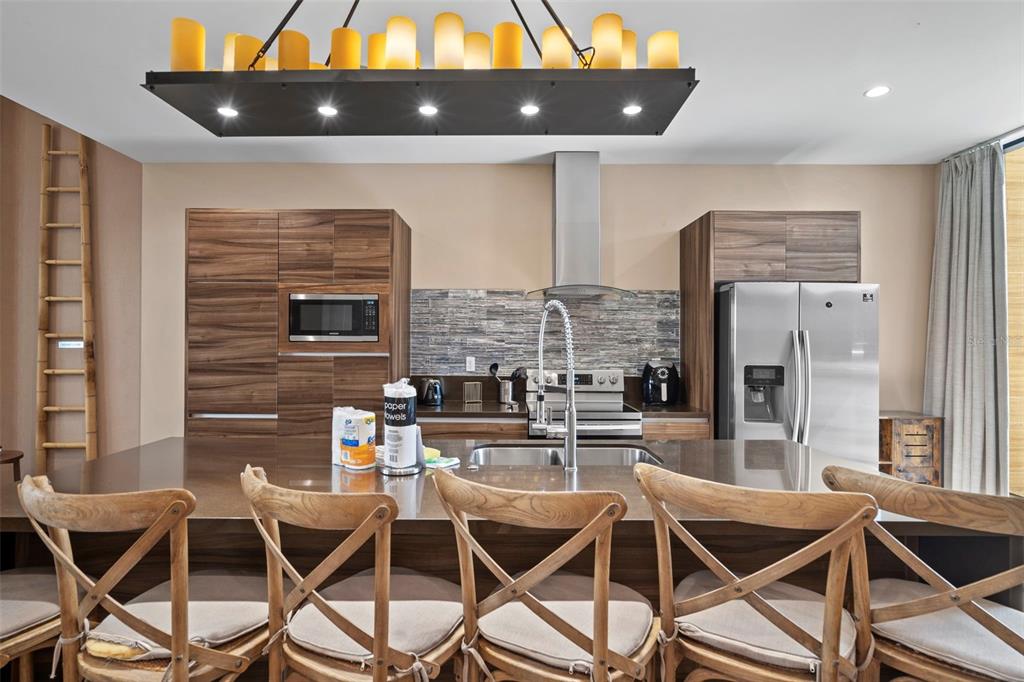A modern kitchen features wood cabinets, a large island with bar seating, and a chandelier — 3099 ROCKEFELLER WAY, KISSIMMEE, FL