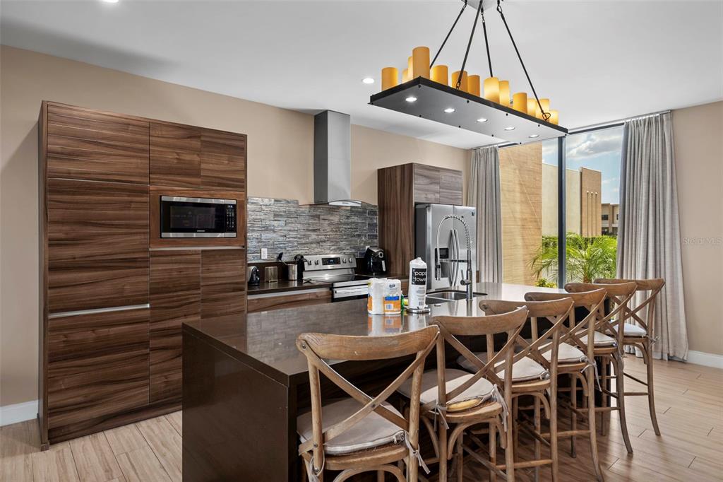 A modern kitchen features dark wood cabinetry, a stone backsplash, and a large island — 3099 ROCKEFELLER WAY, KISSIMMEE, FL