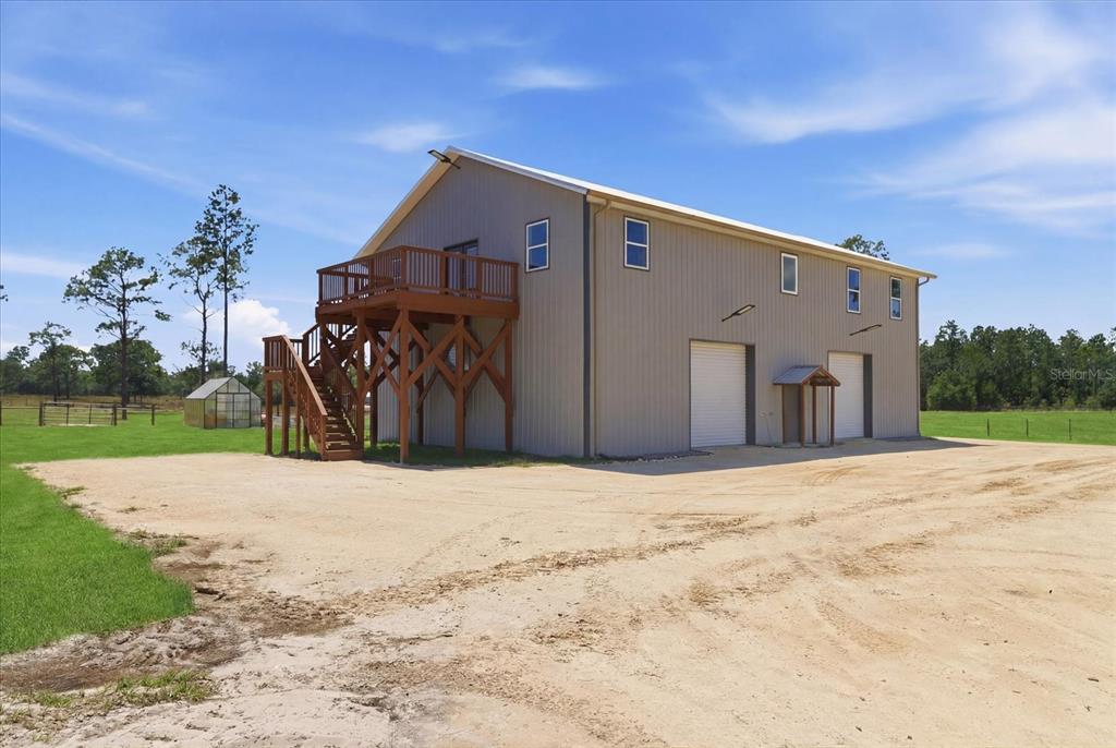 A large metal-sided building features an elevated wooden deck with stairs and two garage doors — 9560 N PARKWOOD AVENUE, DUNNELLON, FL