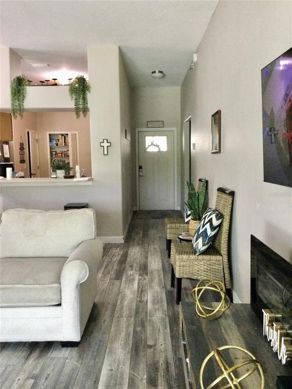 A living room features wood-look flooring, a white sofa, and a hallway leading to an entryway — 10728 SHADY PRESERVE DRIVE, RIVERVIEW, FL