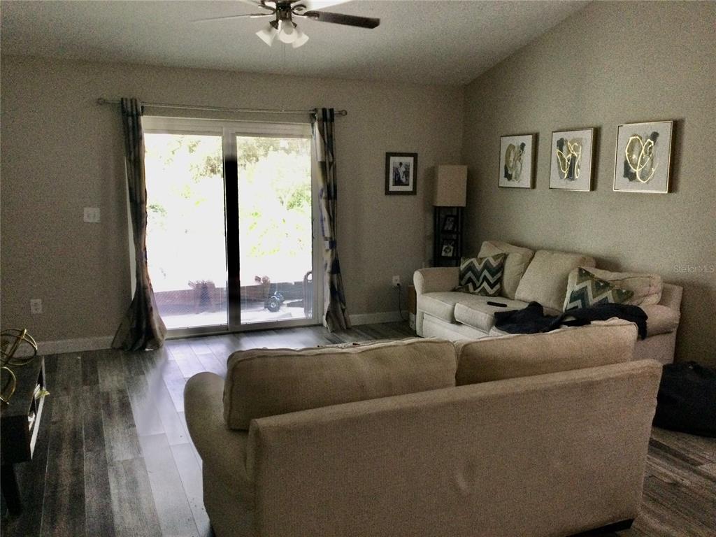 A living room features light-colored sofas, wood-look flooring, and a sliding glass door to outside — 10728 SHADY PRESERVE DRIVE, RIVERVIEW, FL