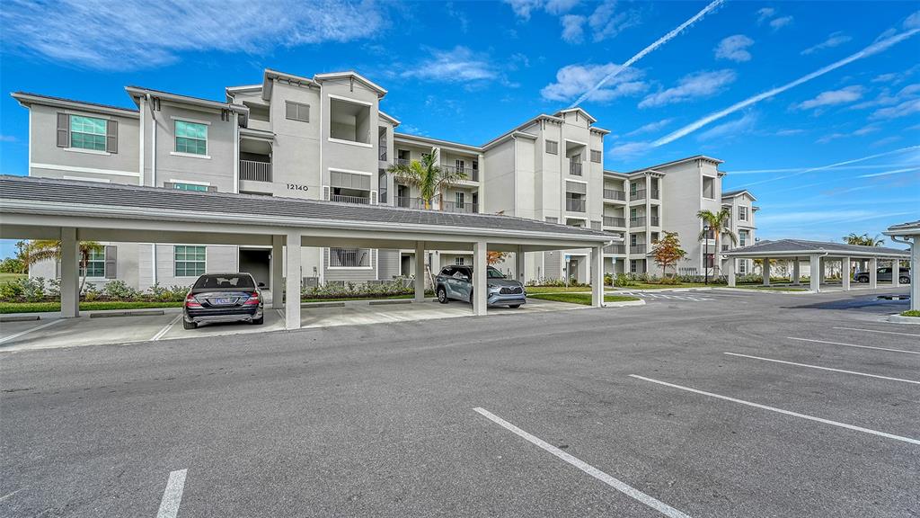 A multi-story apartment building with a covered parking area and two parked cars — 12140 WELLEN GOLF STREET UNIT 307, VENICE, FL