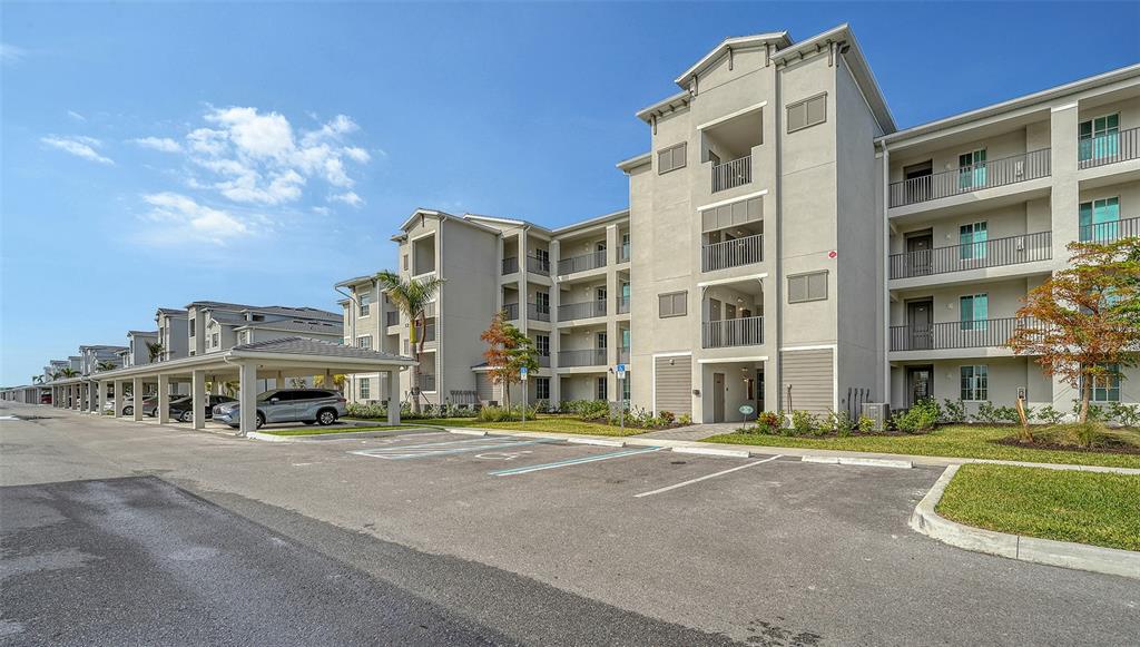 A multi-story apartment building with covered parking and a paved lot in the foreground — 12140 WELLEN GOLF STREET UNIT 307, VENICE, FL