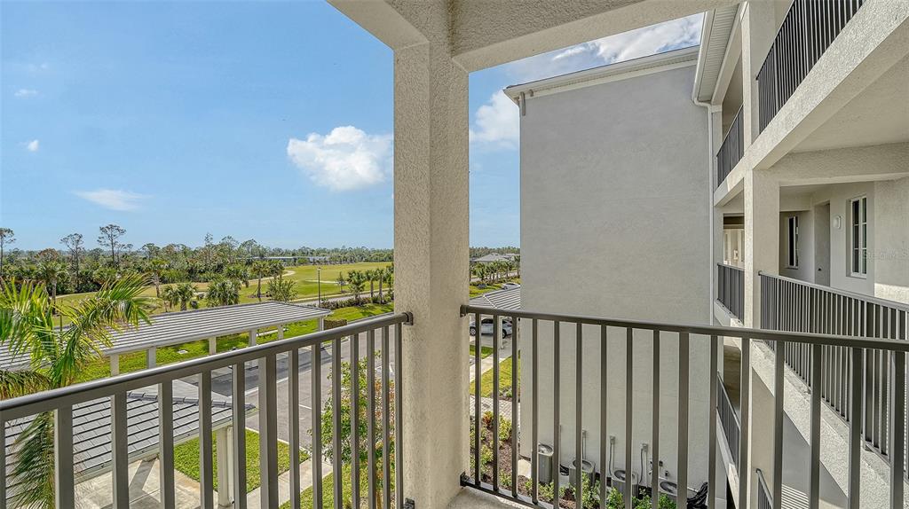 A view from a covered balcony overlooking a parking area, landscaping, and a distant golf course — 12140 WELLEN GOLF STREET UNIT 307, VENICE, FL