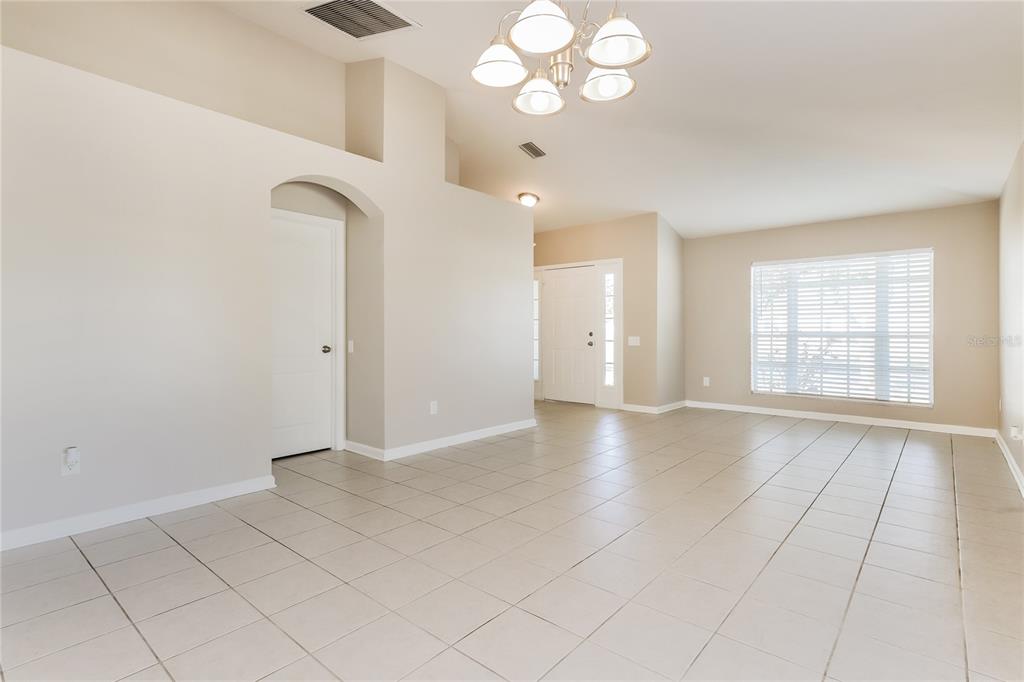 A bright, empty room features light-colored tile flooring, beige walls, and a multi-bulb chandelier — 13302 EVENING SUNSET LANE, RIVERVIEW, FL