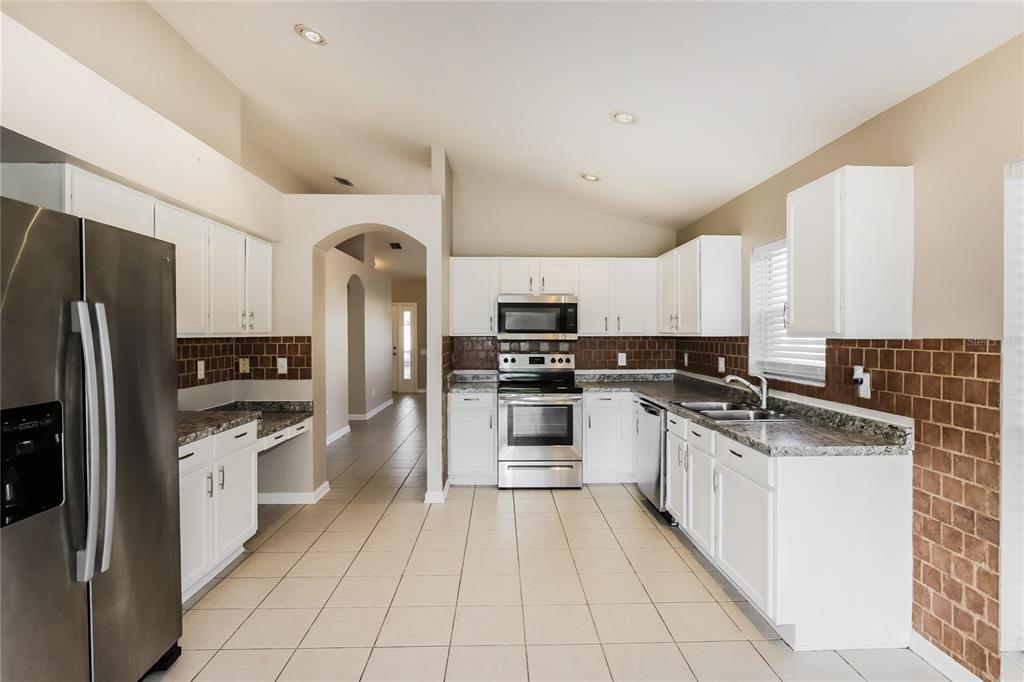 A kitchen features white cabinets, stainless steel appliances, a brown tiled backsplash, and tile flooring — 13302 EVENING SUNSET LANE, RIVERVIEW, FL