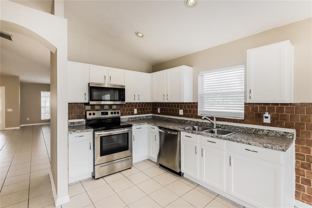 A kitchen features white cabinets, stainless steel appliances, granite countertops, and a brown tiled backsplash — 13302 EVENING SUNSET LANE, RIVERVIEW, FL