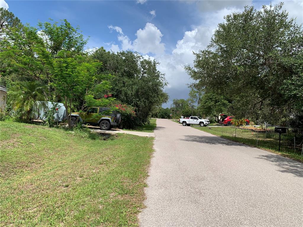 A paved residential street lined with mature trees, parked vehicles, and grassy yards — 17489 CLOVER, PORT CHARLOTTE, FL