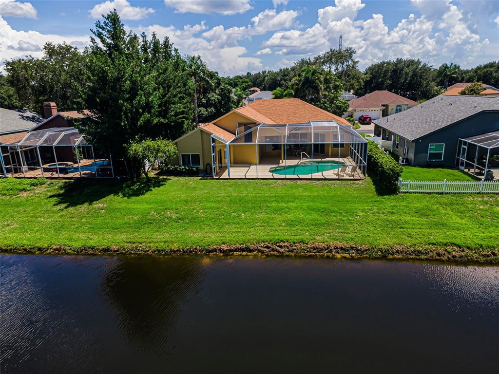 An aerial view of a yellow house with a screened pool enclosure by a lake — 1259 PARADISE LAKE DRIVE, TARPON SPRINGS, FL