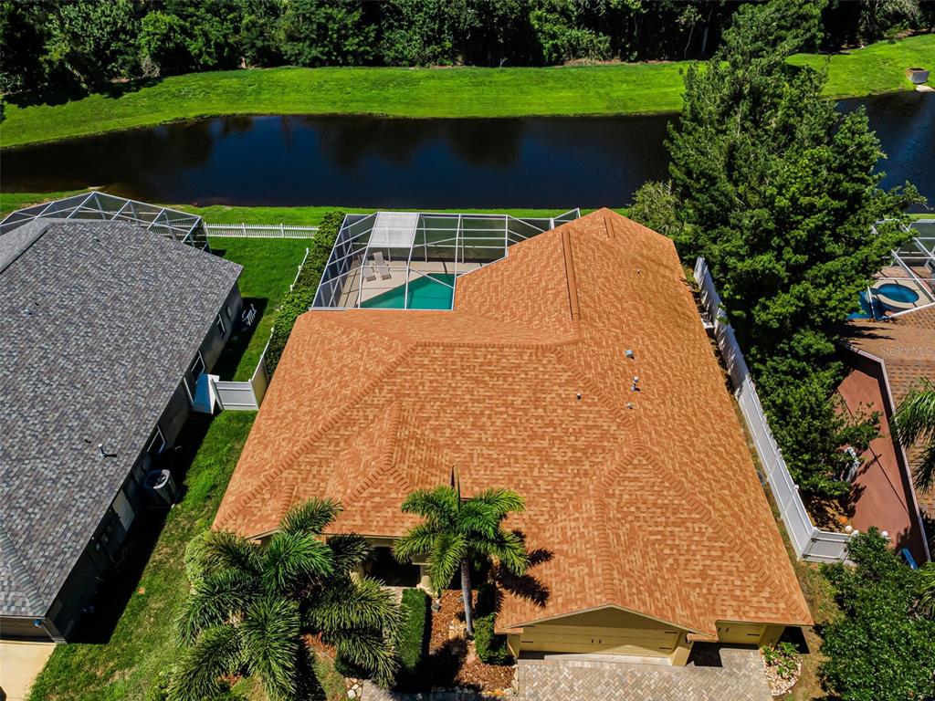 An aerial view shows a house with a tan shingle roof, pool cage, and palm trees — 1259 PARADISE LAKE DRIVE, TARPON SPRINGS, FL