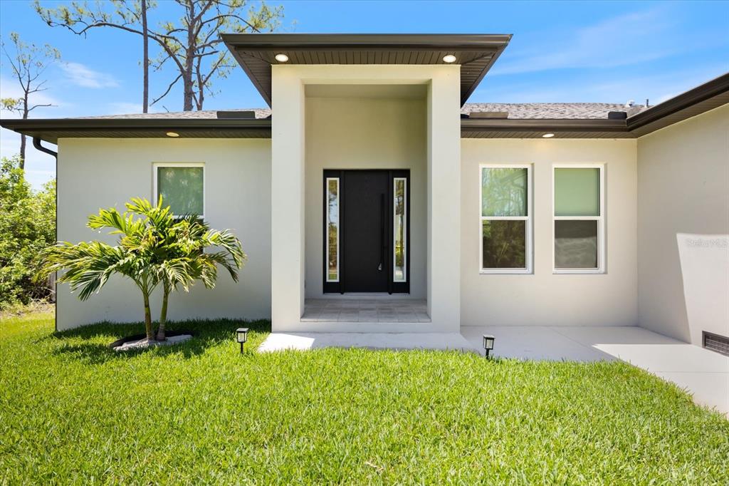 The exterior of a modern house features a covered entryway with a dark front door — 12133 FEDERAL AVENUE, PORT CHARLOTTE, FL