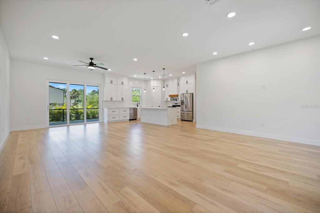 An open-concept kitchen and living area features light wood flooring, white cabinetry, and sliding doors — 12133 FEDERAL AVENUE, PORT CHARLOTTE, FL