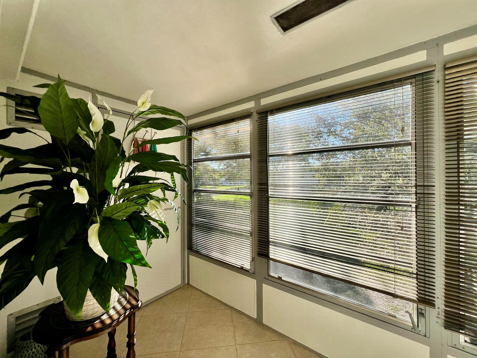 A sunroom features tile flooring, a large peace lily plant, and windows with horizontal blinds — 180 Tilford I, Deerfield Beach FL 33442, DEERFIELD BEACH, FL