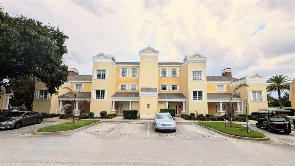 A yellow multi-story apartment building features a central tower and a paved parking lot — 1338 SEVEN EAGLES COURT UNIT 202, REUNION, FL