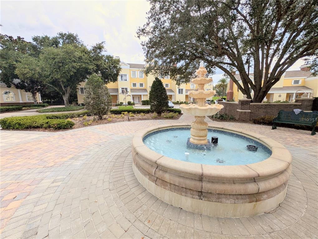 A tiered stone fountain sits in the center of a paved courtyard near residential buildings — 1338 SEVEN EAGLES COURT UNIT 202, REUNION, FL